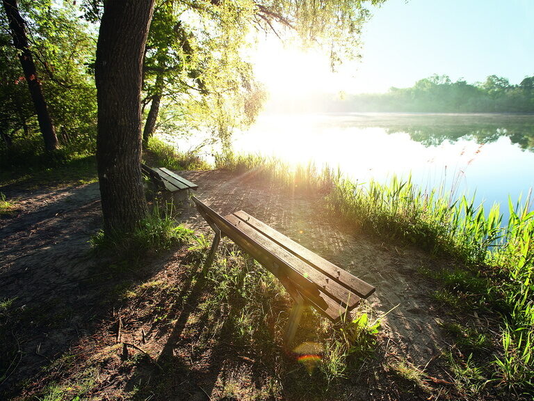 Eine gemütliche Bank zum sitzen mit Blick auf den blau schimmernden sonnenbeleuchteten Inn von Bad Füssing.