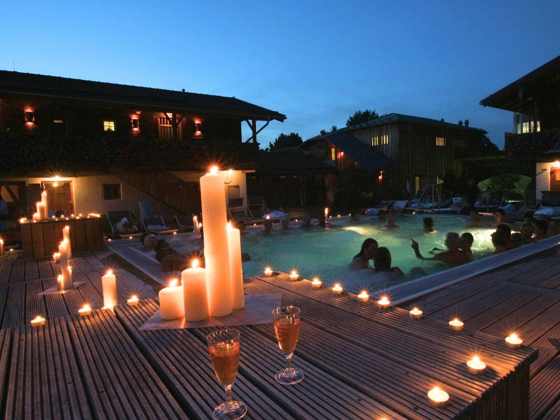 Ein hölzernes Deck mit Kerzen vor einem beleuchteten Pool bei Nacht für ein einzigartiges Saunaerlebniss in Bad Füssing.