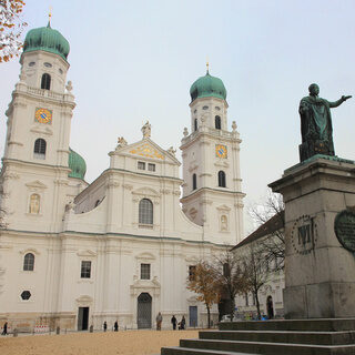 Eine Bronzeskulptur steht auf dem Domplatz vor dem kirchlichen Wahrzeichen, dem Stephansdom in Passau.