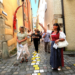 Eine Gruppe von Menschen spaziert durch die bunte Kopfsteinpflasterstraße in Passaus Altstadt.
