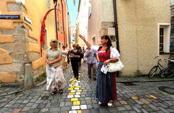 Eine Gruppe von Menschen spaziert durch die bunte Kopfsteinpflasterstraße in Passaus Altstadt.